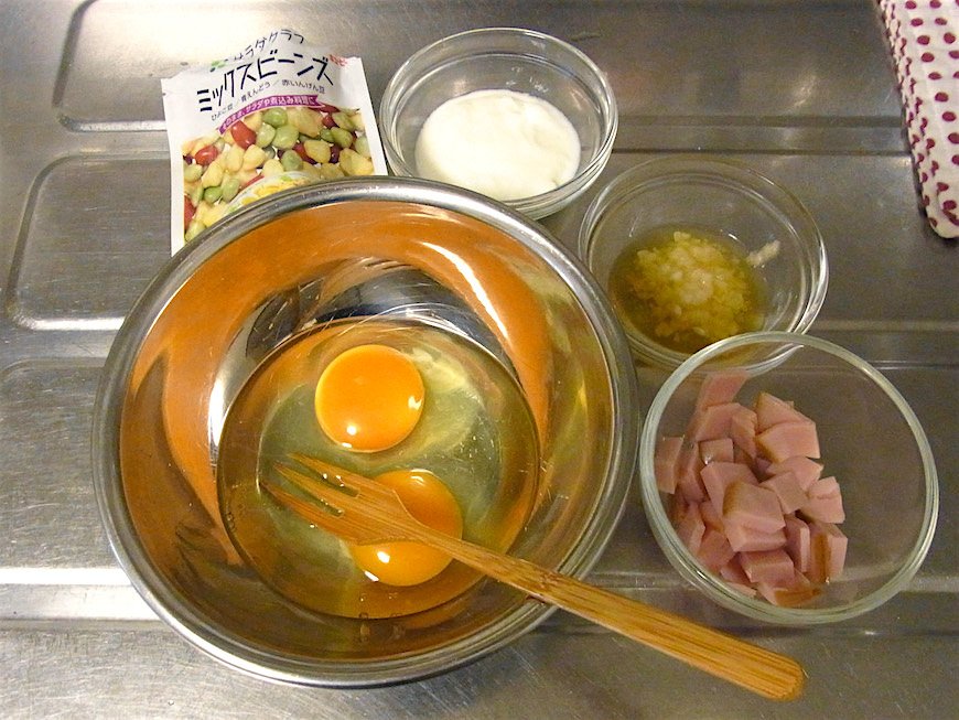 卵を割りほぐし、分量のヨーグルト、塩麹、みりんを入れて混ぜ、ミックスビーンズとハムも入れて混ぜる