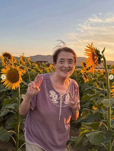 夕日に照らされたひまわり畑でピースする84歳のおばあちゃん