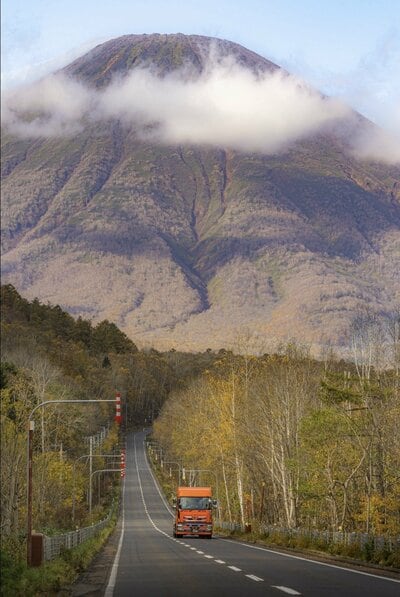 雲をまとう羊蹄山と色づいた木々の間を延びる道