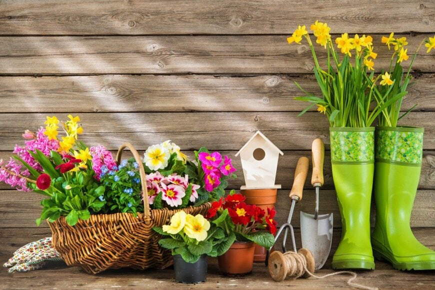緑のブーツに黄色い花が挿してある。横にはスコップや春の花が植わったバスケット。