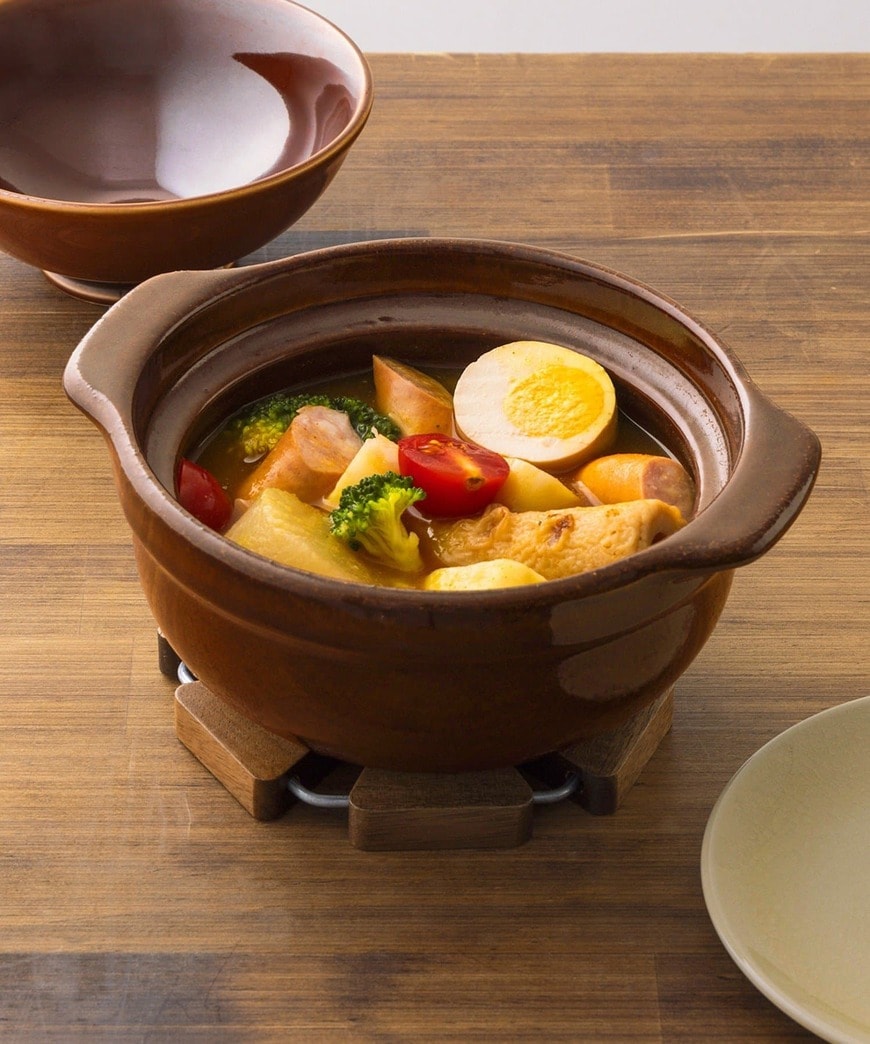 鍋敷きにのせた茶色い鍋と、卵や野菜の入った料理