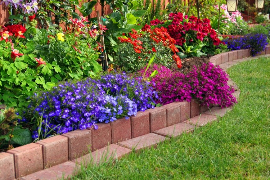 レンガで縁取られた花壇。紫や赤い花が植えられている。