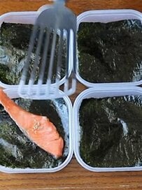 タッパー容器を用いて4人分の海苔鮭弁当を実際に作ってみた。海苔を敷いたご飯の中央に鮭を配置し、複数人分のおかずを効率よく詰める実践的なお弁当術