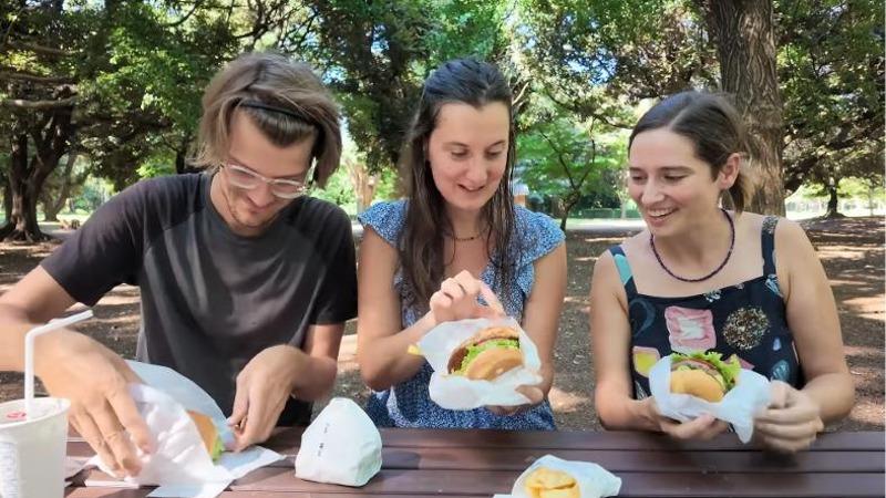 公園のテーブルでハンバーガーの包みを開く3人