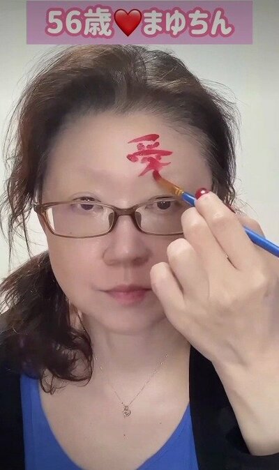 額に筆で赤い文字を描く様子