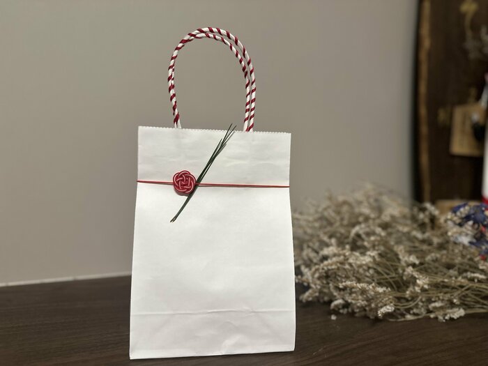 持ち手へ赤い紐を巻きつけると、シンプルな紙袋がよりギフト用の装いに
