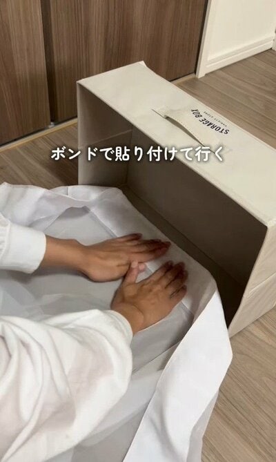 カーテンを半分に折り、ボンドで収納ボックスの内側に貼り付けていく様子。