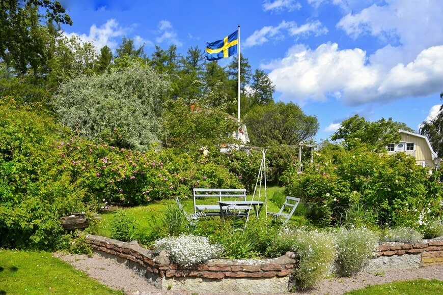 スウェーデンの国旗が揚がっている、バラなどの花が咲く庭 