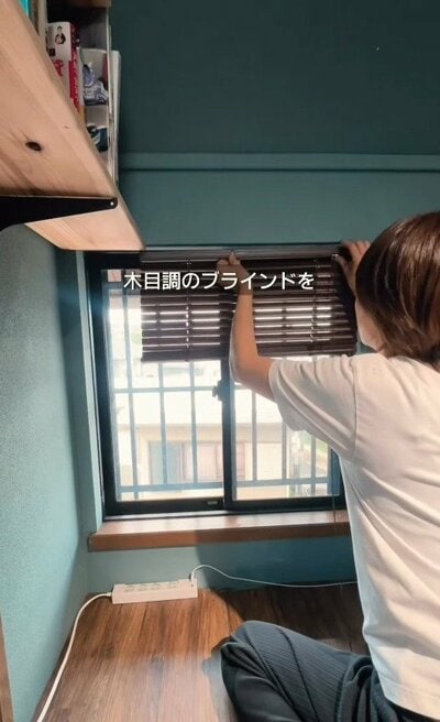 窓に木目調のブラインドを当てて、サイズが合わないか確認している様子