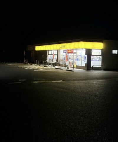 夜の駐車場の先で黄色く光るコンビニの看板