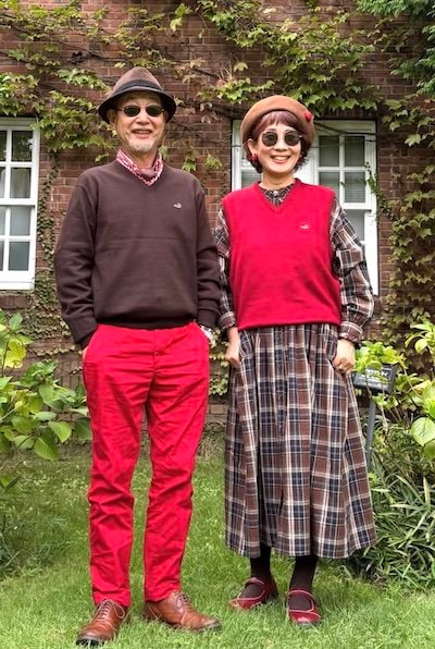 ブラウンのニットに赤パンツを合わせた夫と赤ベストの奥さま