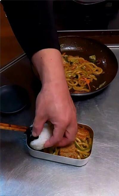 焼きうどんの上に、のりを巻いたおにぎりがのせられるところ