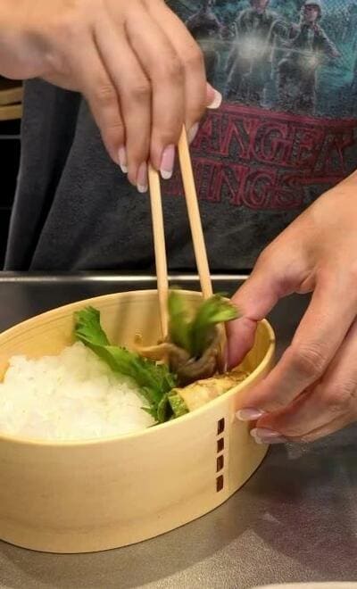 ご飯の横に敷いた緑の葉の上へ、肉巻きを箸で詰めていく