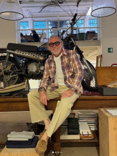 バイクの前に座る、チェックシャツとベージュパンツのコーデ