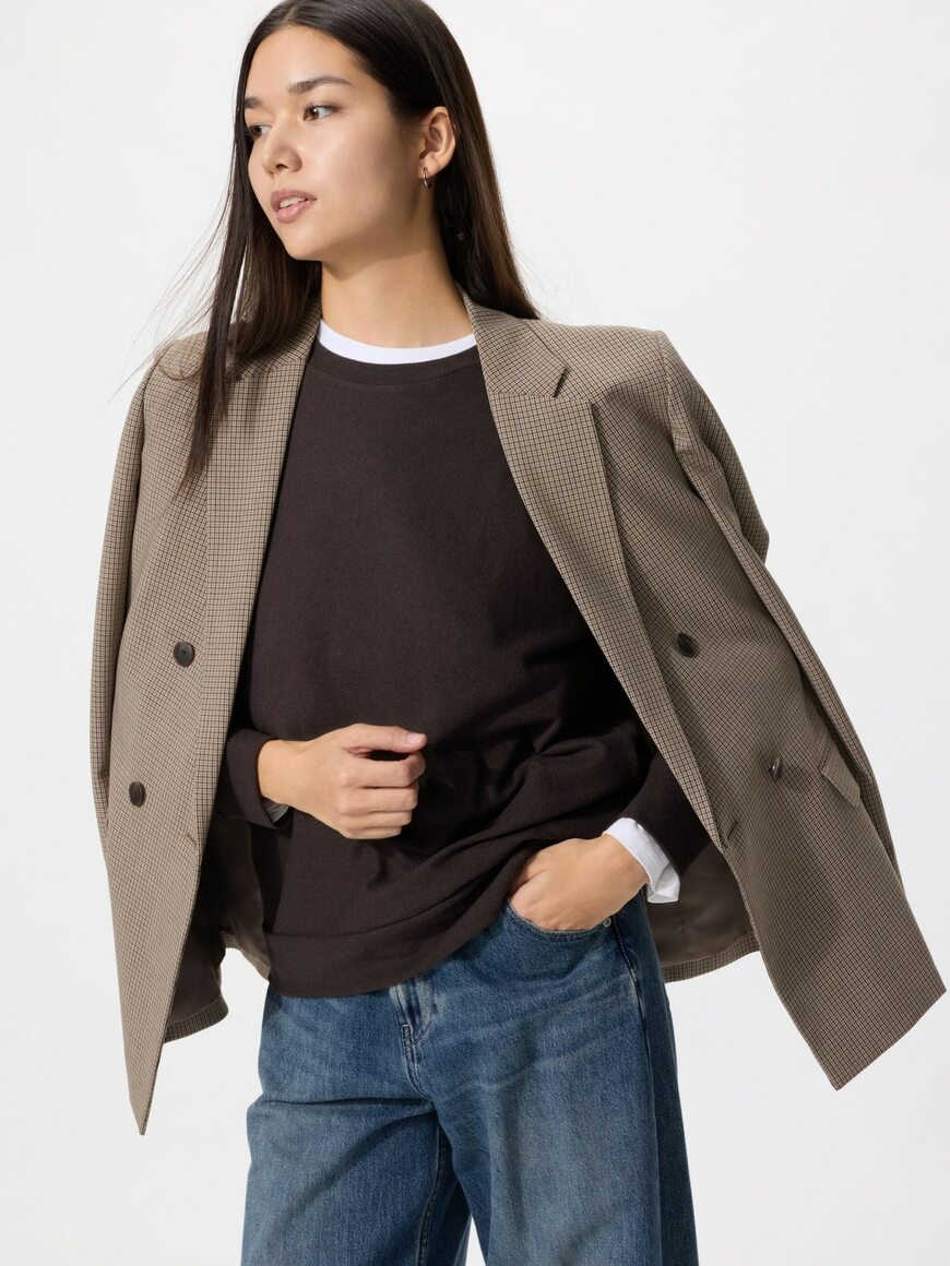 ダークブラウンのソフトニットフリースクルーネックTを着て、ジャケットを肩に掛けた女性