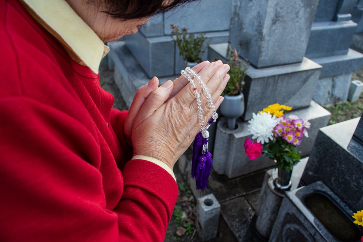 お墓の前で手を合わせる女性。赤いセーターを着ている
