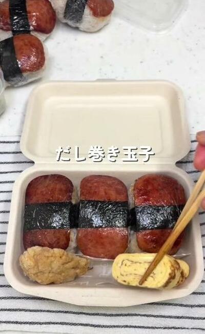 奥にスパムおにぎりが3つ並び、手前にだし巻き玉子が詰められていくところ