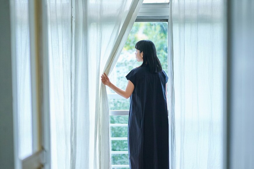 カーテンを開けて外を見る女性の写真