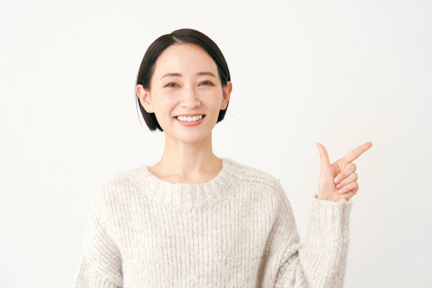 白いセーターを着たショートヘアの美しい女性が笑顔でこちらを向いている。