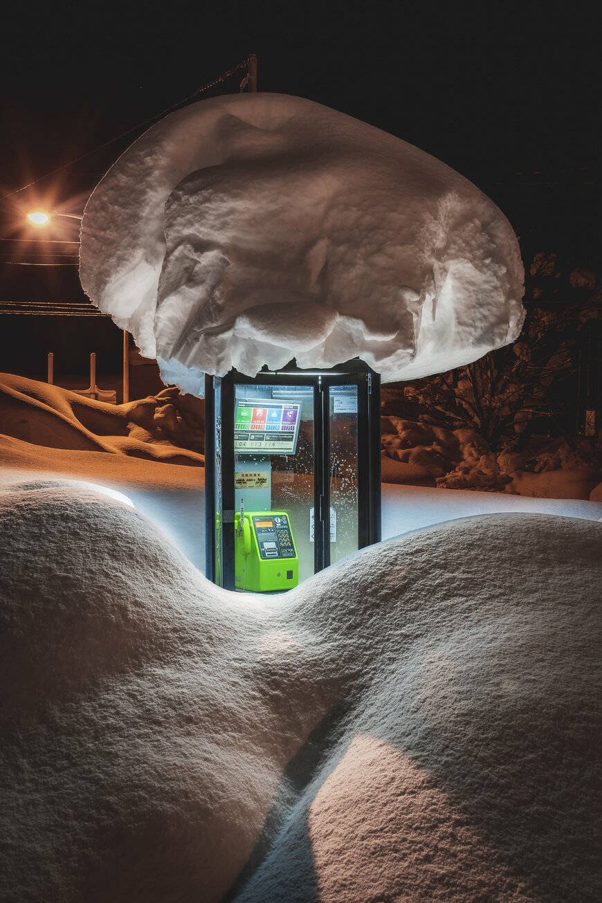 大きな雪の塊を乗せた電話ボックス