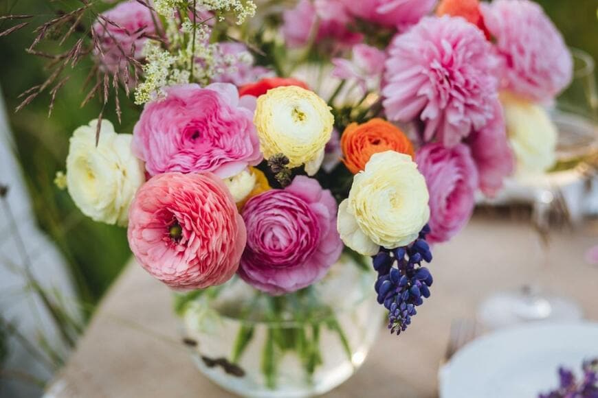 バラやラナンキュラスの花がガラスの花瓶に生けられている。